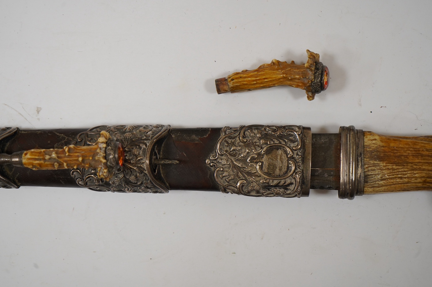 A Scottish Highland dirk, c.1900, regulation blade, staghorn handle with white metal mounts and foiled glass pommel stone, leather covered scabbard with white metal mounts embossed with thistles, containing knife and for